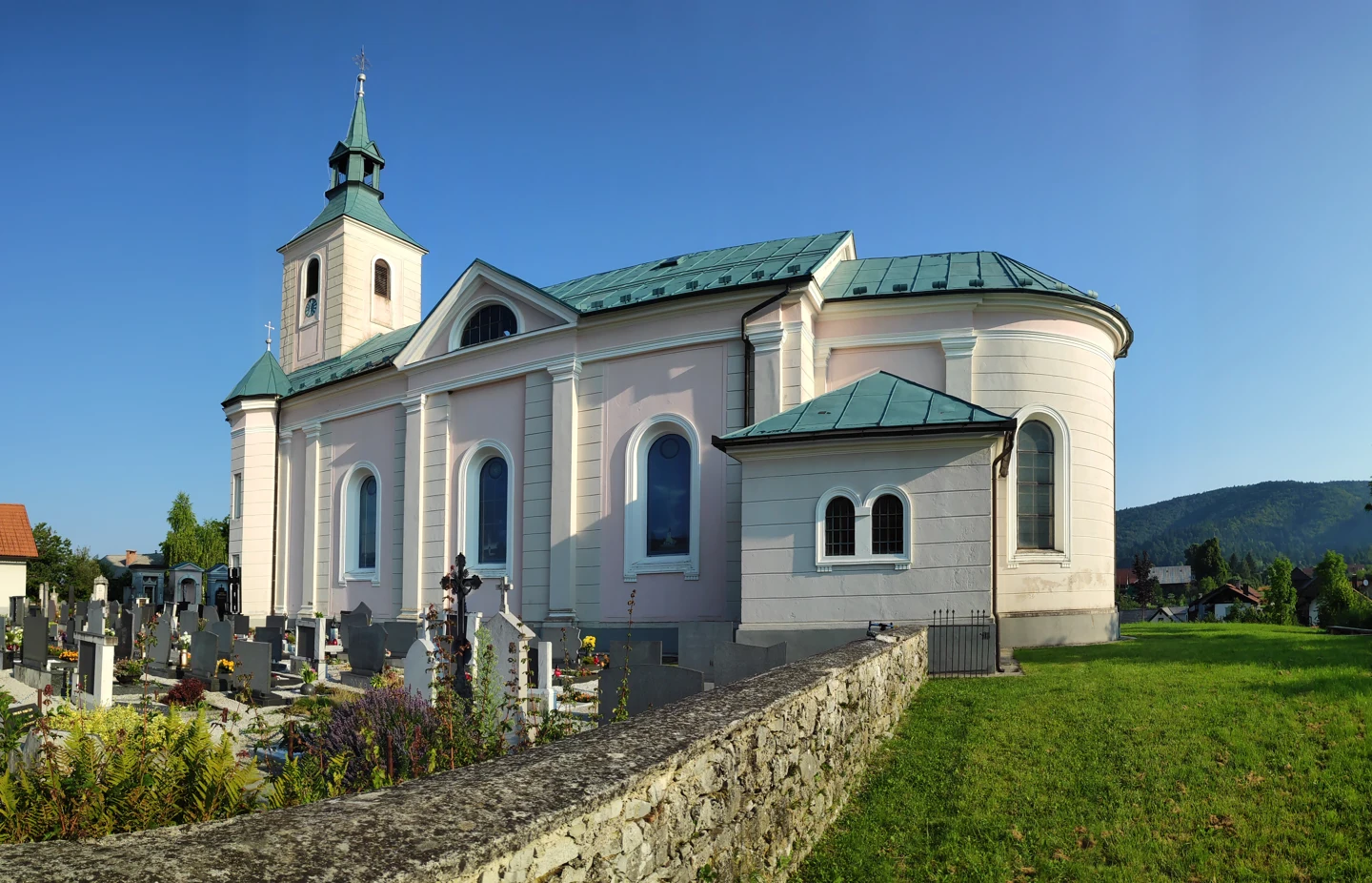 Cerkev sv. Jerneja v Begunjah pri Cerknici ob pokopališču, z zvonikom in zaobljenim stavbnim delom.