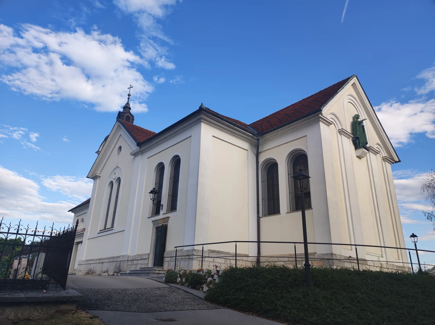 Svetla cerkev Marijinega vnebovzetja v Domžalah z visokimi okni, rdečo streho in kipom Kristusa na vzhodni fasadi.