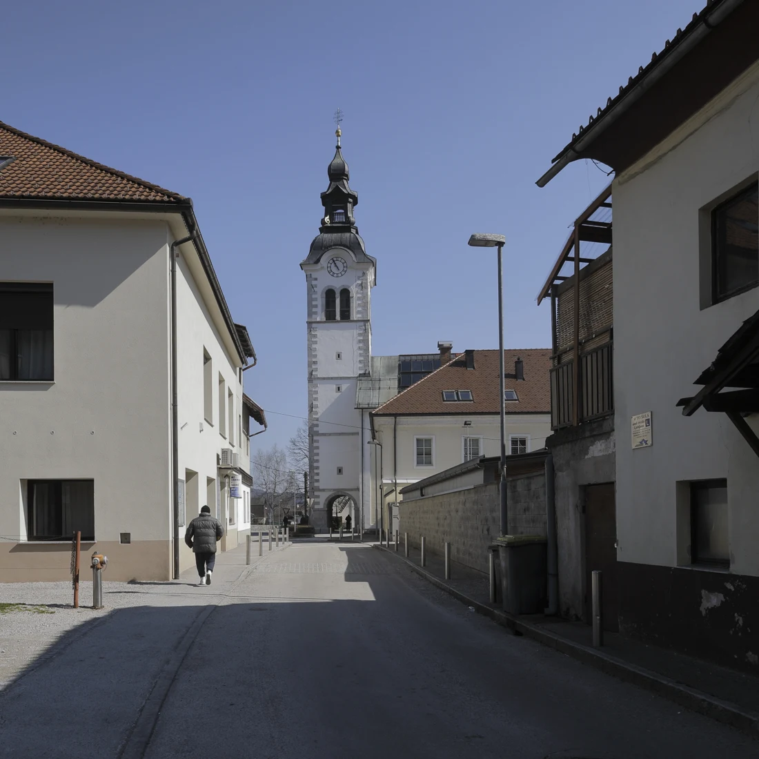 Zvonik cerkve sv. Martina z uro in razčlenjeno streho ter vhod pod njim, viden med hišami ob Troštovi ulici na Igu.