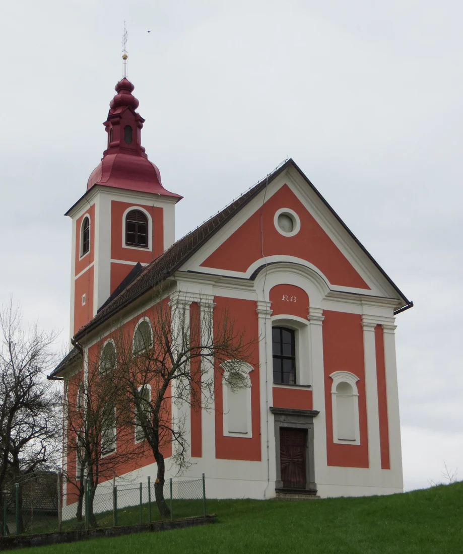 Rdeče-belo pročelje cerkve sv. Gregorja s kamnitim portalom, pilastri in nišami, zadaj zvonik na Dobravici.