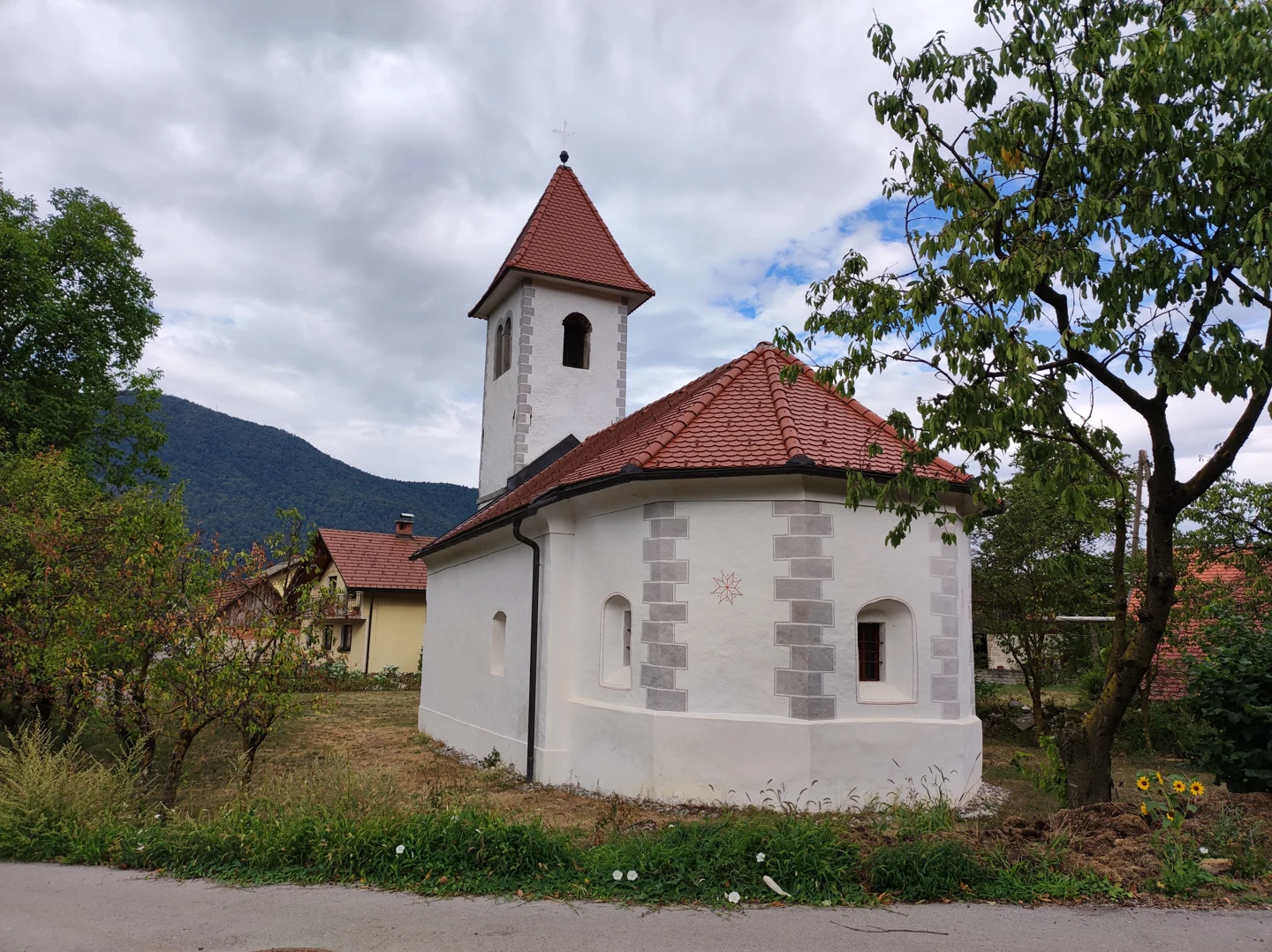 Bela cerkev sv. Mihaela z mnogokotnim prezbiterijem, rdečo streho in zvonikom ob drevju v Iški vasi.