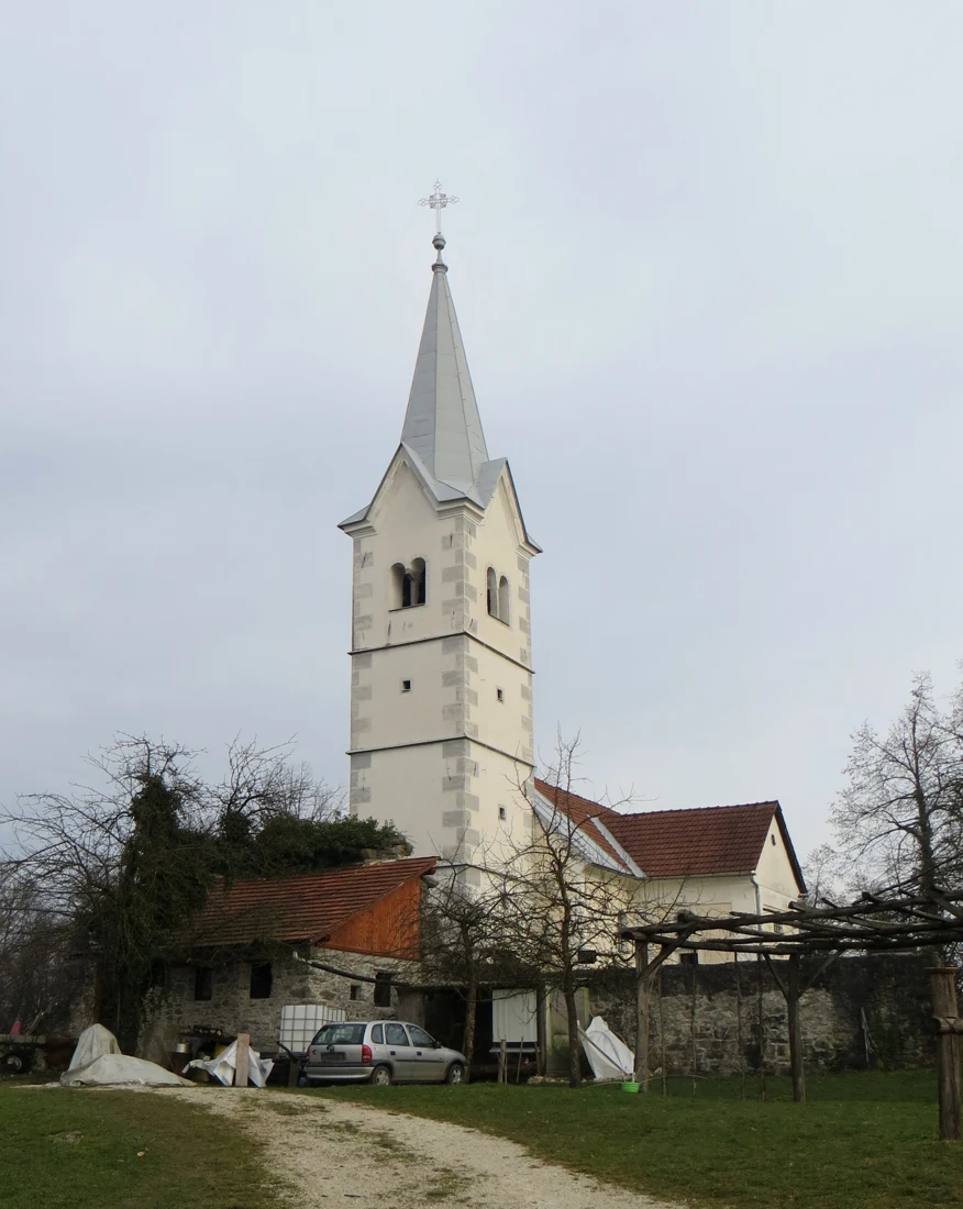 Cerkev sv. Kunigunde na Taboru z visokim svetlim zvonikom in rdečimi strehami nad kamnitim obzidjem.