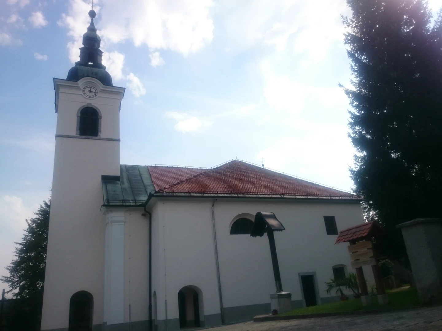 Cerkev sv. Nikolaja v Bizoviku z visokim zvonikom, številčnico in razpelom pred stransko steno