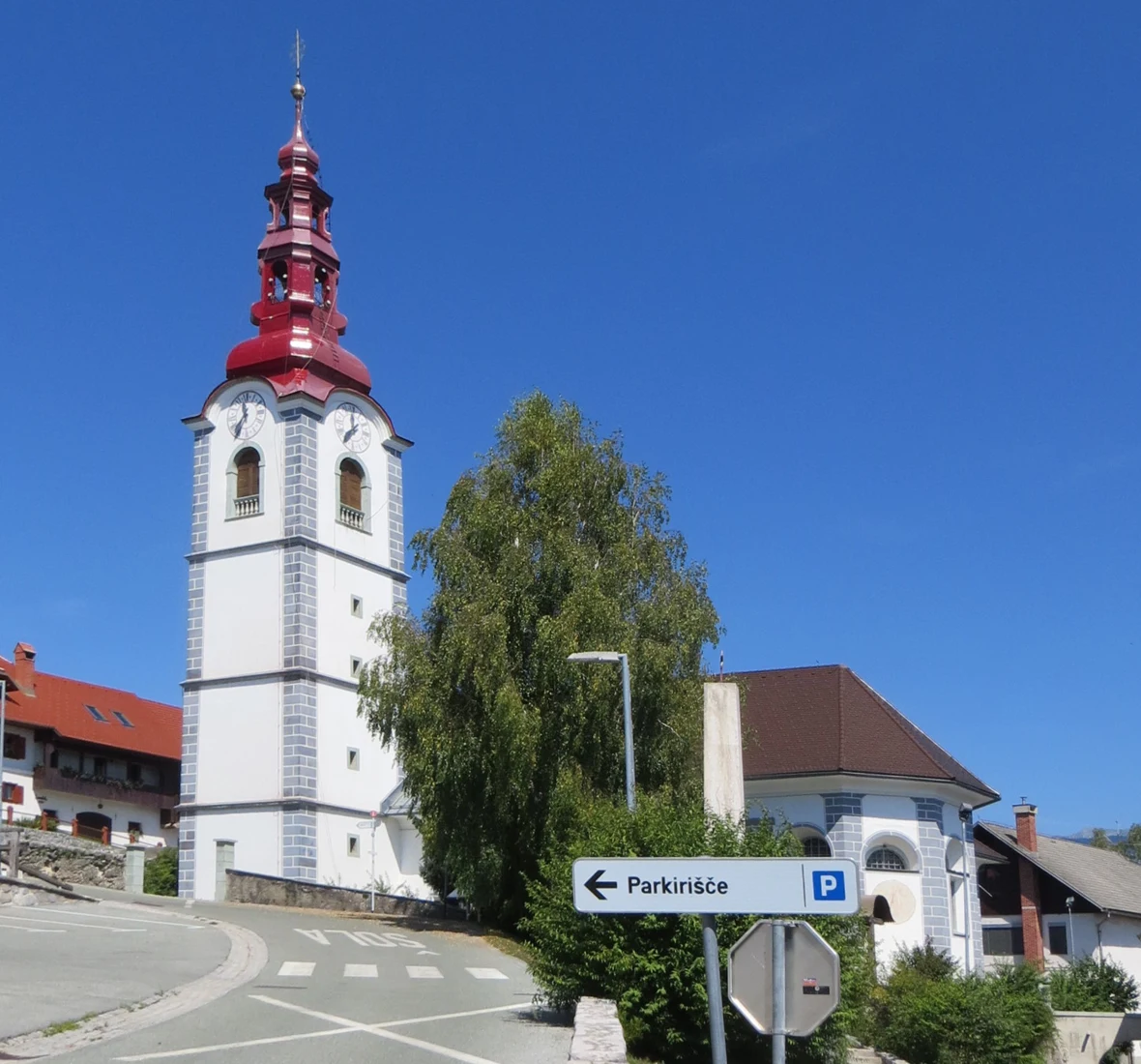 Cerkev Marije Pomočnice v Ljubnem z visokim svetlim zvonikom in razčlenjeno rdečo streho