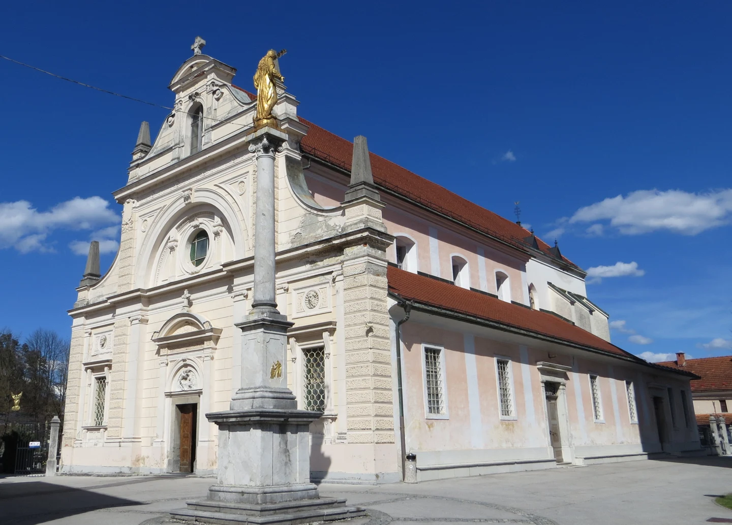 Zahodno pročelje in stranska ladja cerkve sv. Mihaela v Mengšu z Marijinim znamenjem pred vhodom.
