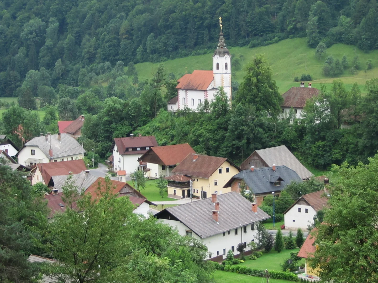 Oddaljeni pogled na cerkev sv. Brikcija nad hišami Podlipe, junij 2012