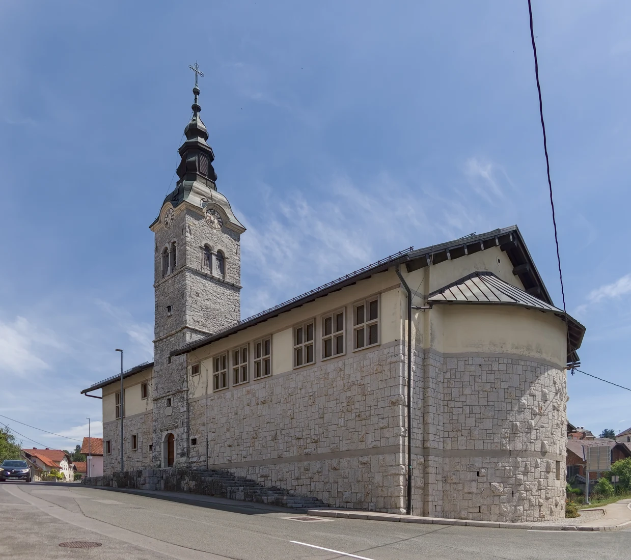 Kamnita cerkev Srca Jezusovega na Rakeku ob cesti, z zvonikom in dolgo ladjo.