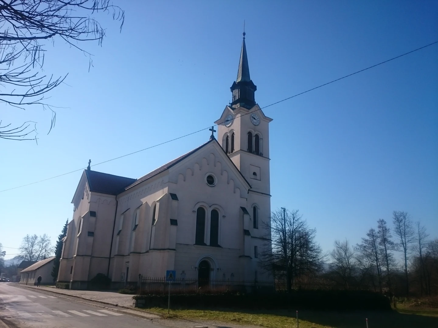 Cerkev sv. Lenarta v Sostrem ob cesti, z visokim zvonikom in polkrožnimi okni.