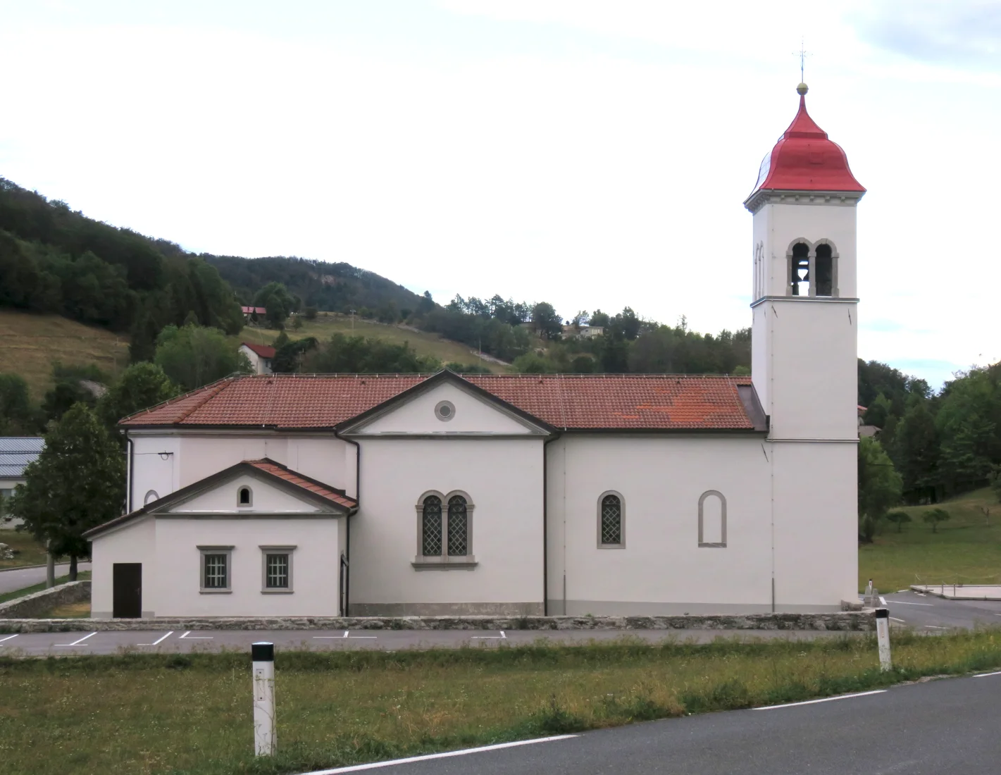 Cerkev Angelov varuhov na Otlici z dvojno obokanim stranskim oknom in kvadratnim zvonikom z rdečo streho.
