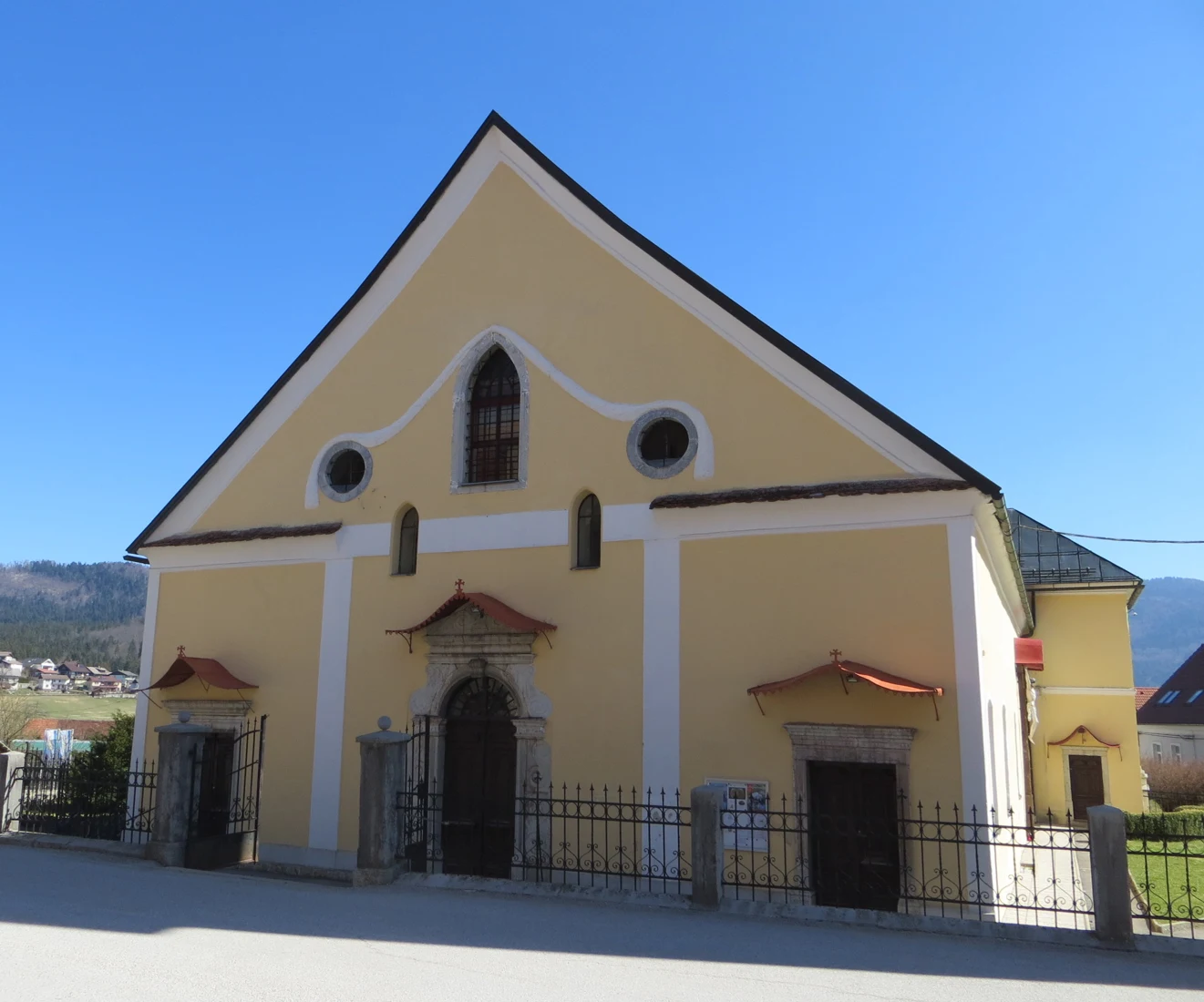 Široko pročelje cerkve sv. Jurija v Starem trgu pri Ložu s tremi kamnitimi portali