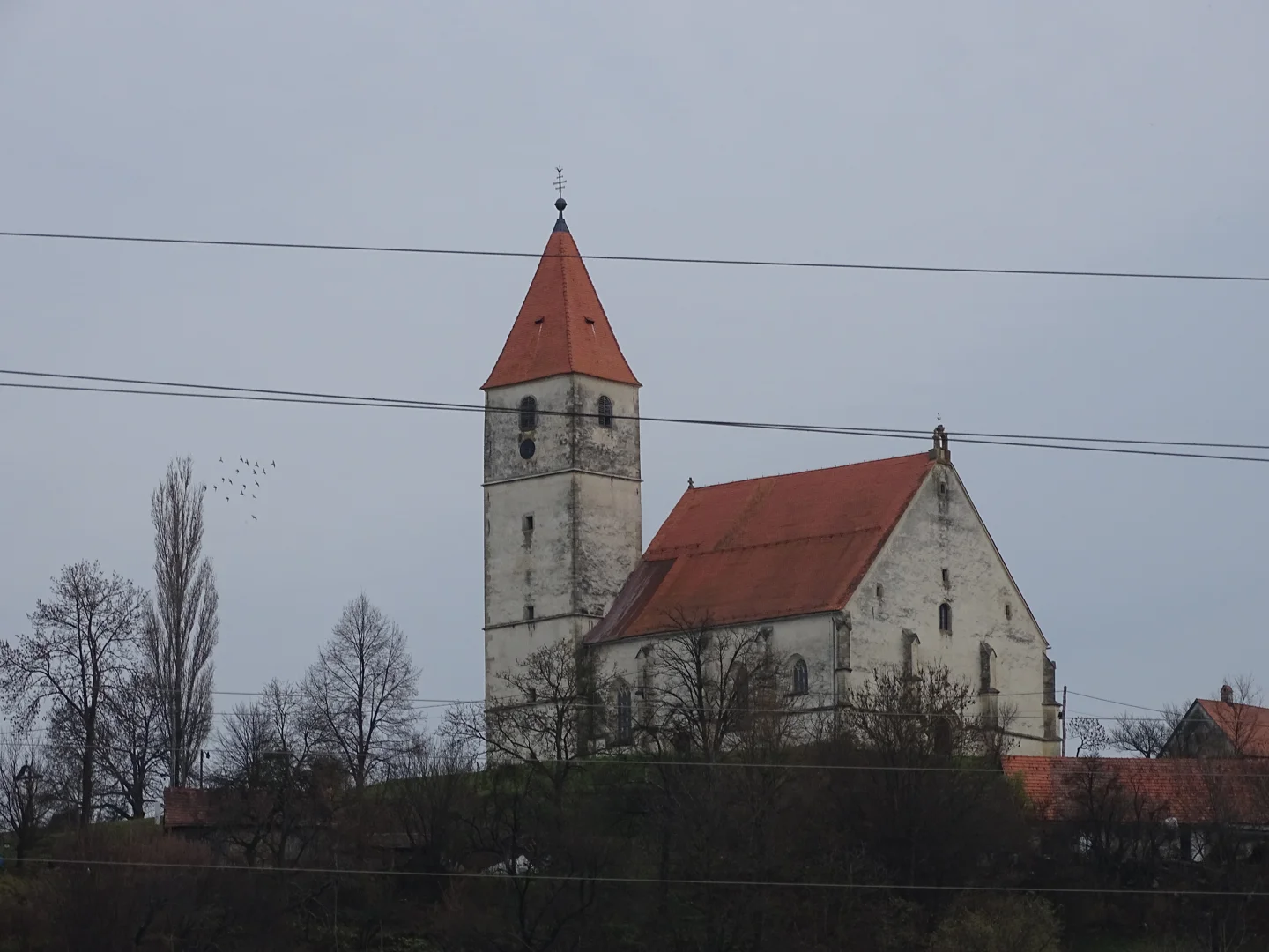 Cerkev sv. Treh kraljev z rdečo streho, oporniki in visokim kvadratnim zvonikom.
